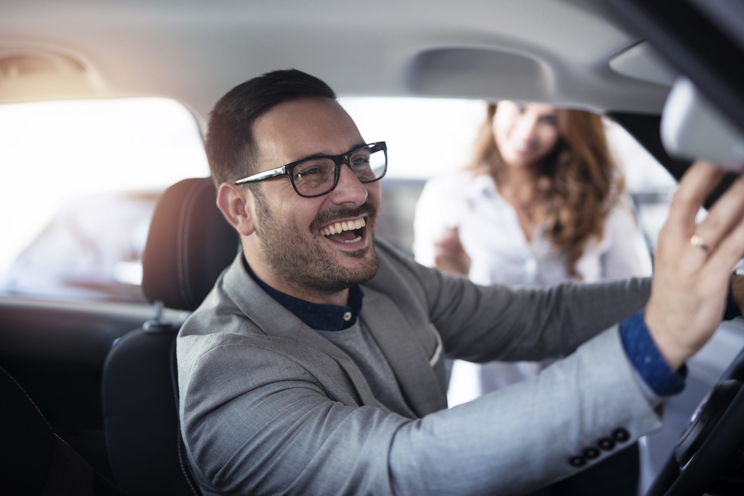 A man with glasses smiling in a car.