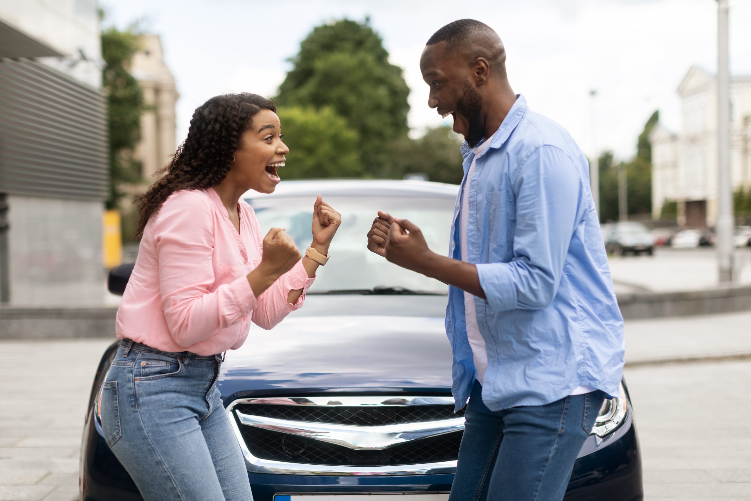 An excited man and woman cheering in front of a new dark blue car.
