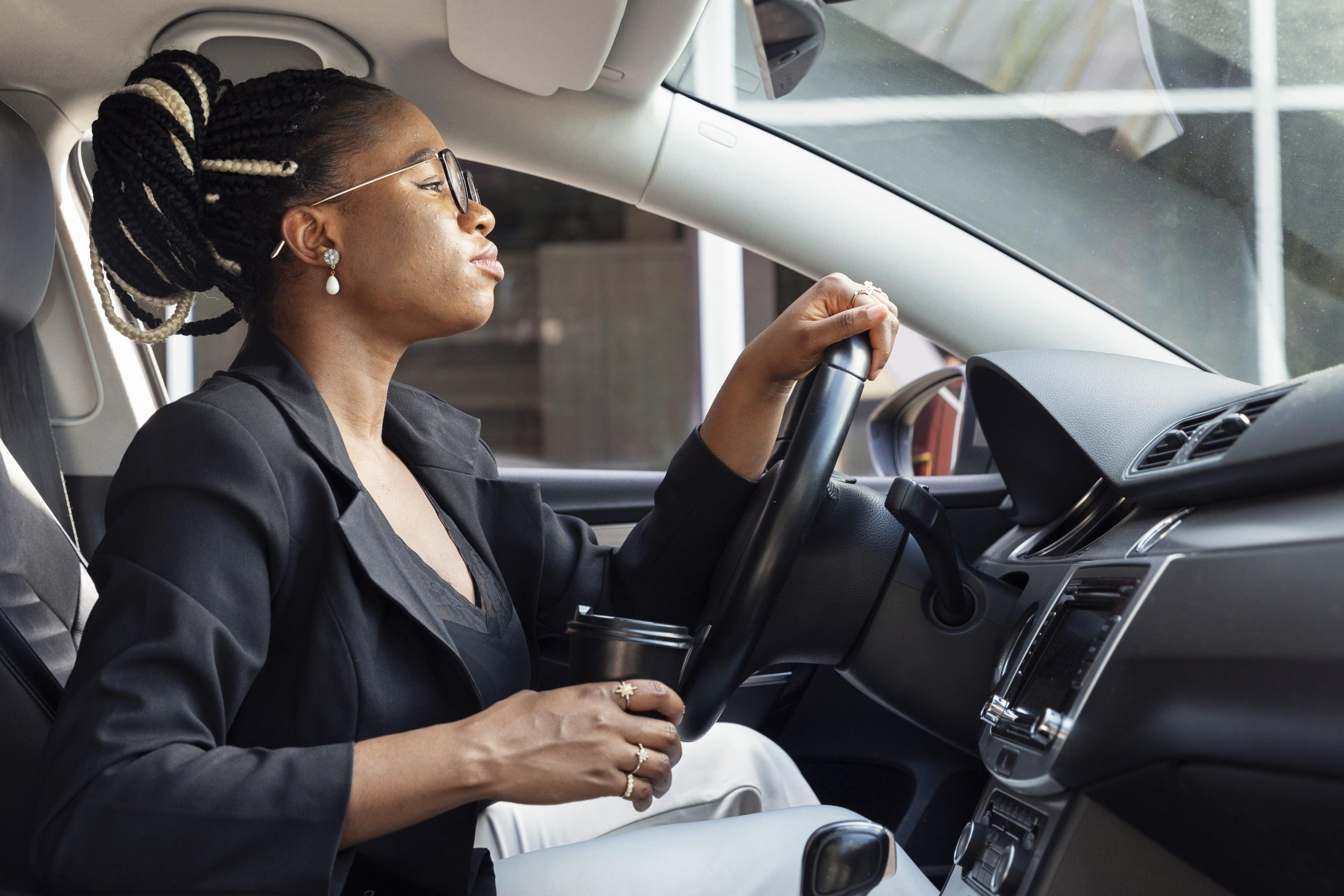 A woman holding a cup in the driver seat of a car