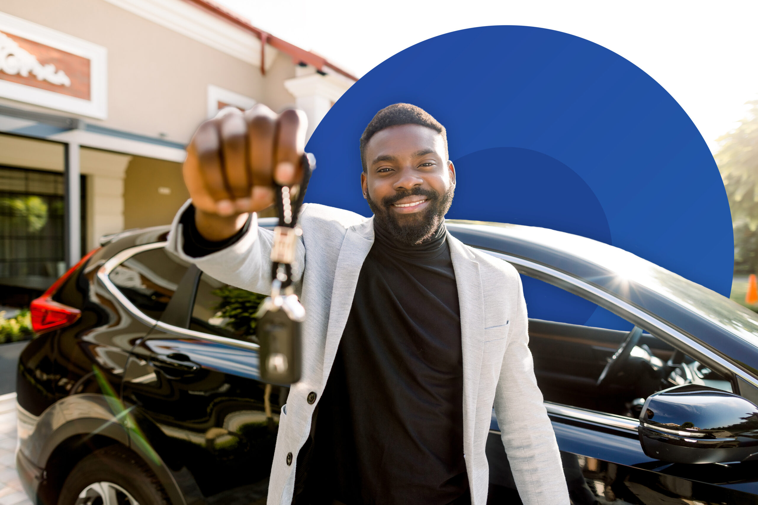 Happy man holding up car keys in front of a new black car
